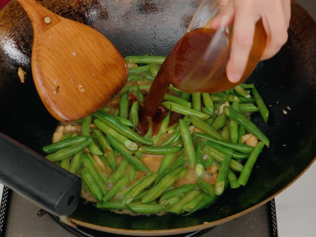 stir fy sauce being poured into a wok full of green beans