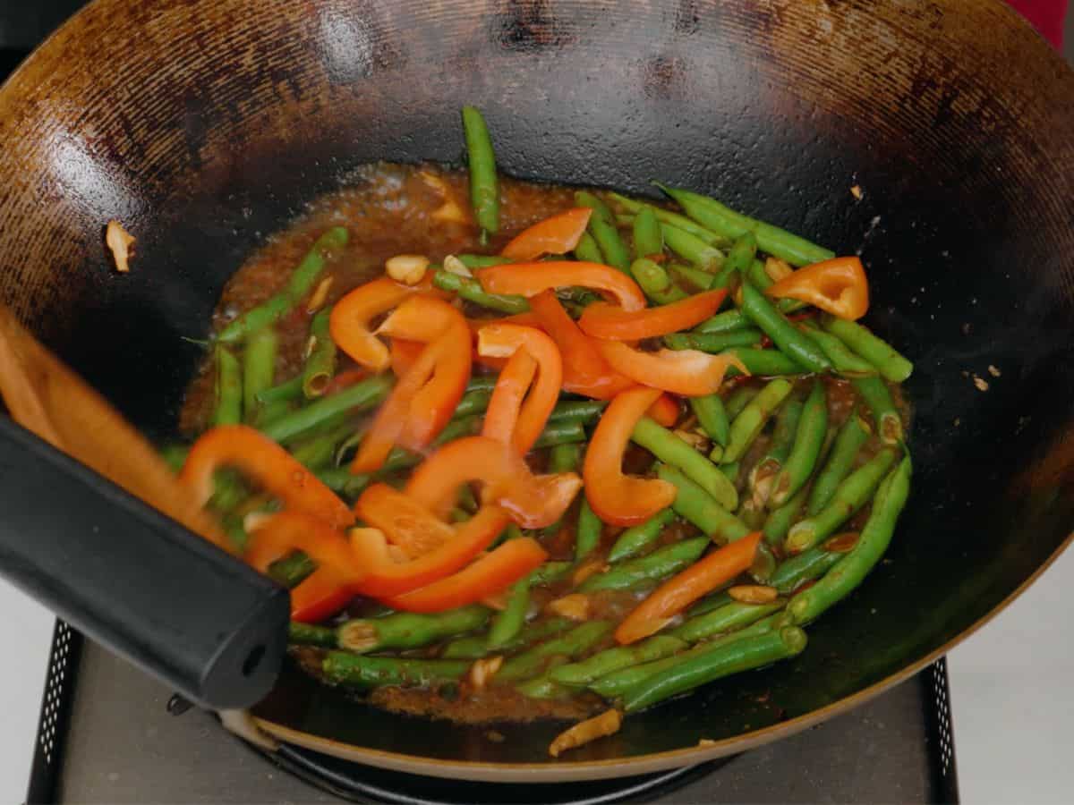 Bell pepper and green beans in a sauce in a wok.