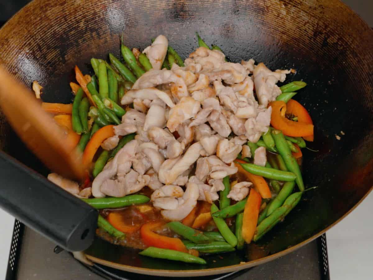 Bell pepper and green beans and chicken in a sauce in a wok.