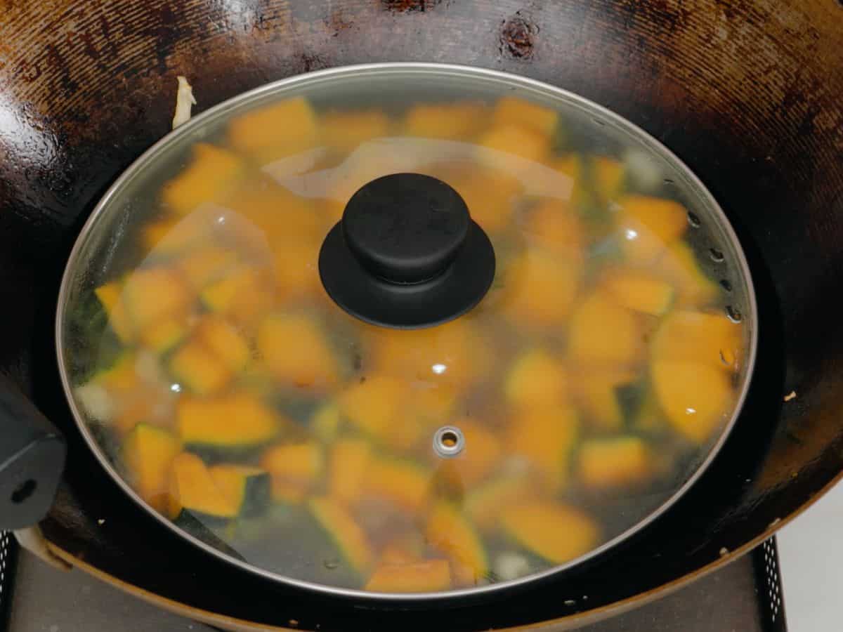 kabocha squash in a wok with a lid over it