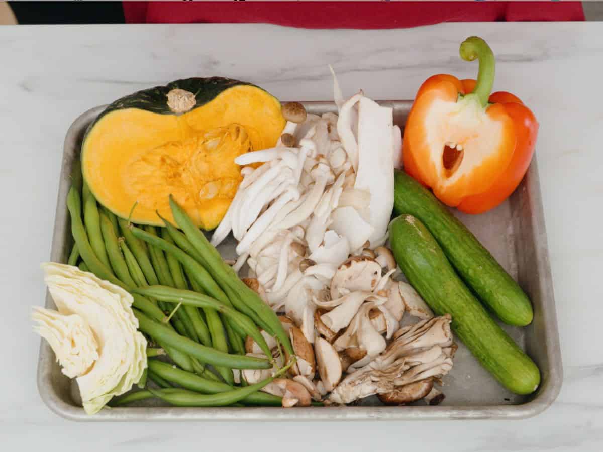a bell pepper, cucumber, squash, mushrooms, green beans and cabbage on a tray