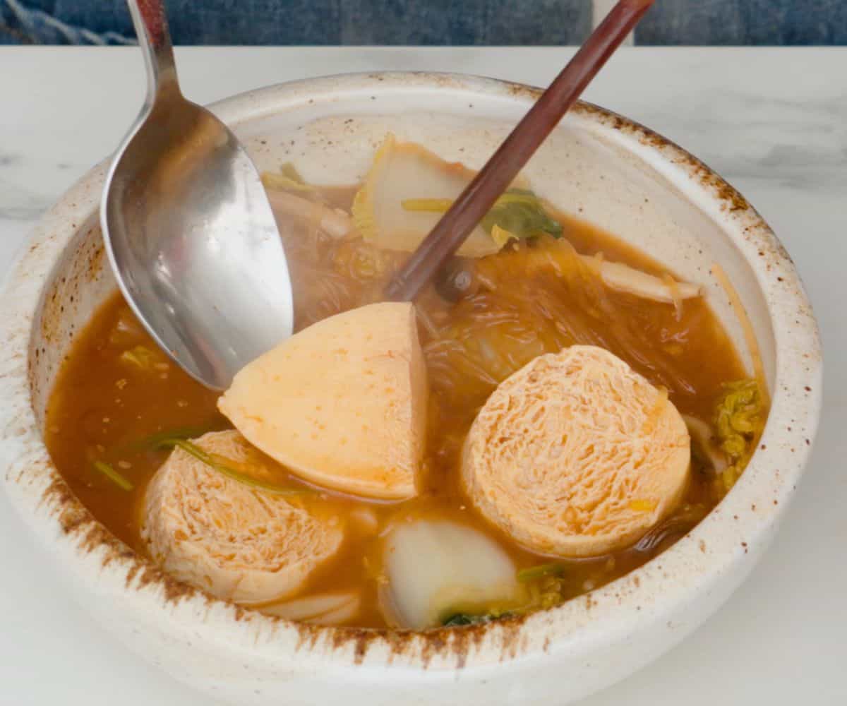 previously frozen silken tofu in a Thai sukiyaki soup in a bowl.