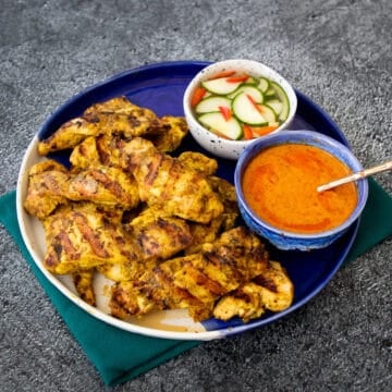 A plate of chicken satay with a bowl peanut sauce and a bowl cucumber pickle.