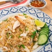 A plate of crab fried rice with cucumber and lime on the side, with a little bowl of fish sauce and chilies condiment