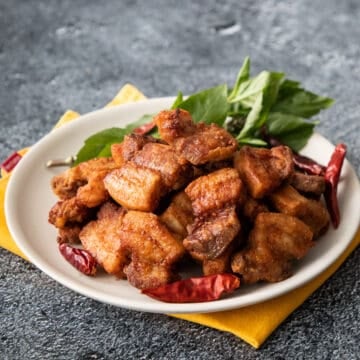 a plate of Thai crispy pork belly with dried chilies and thai basil garnish