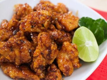 a plate of fried chicken in sweet chili lime sauce and a wedge of lime and makrut lime leaves