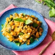 kabocha squash stir fry with eggs and Thai basil on a blue plate on a pink napkin