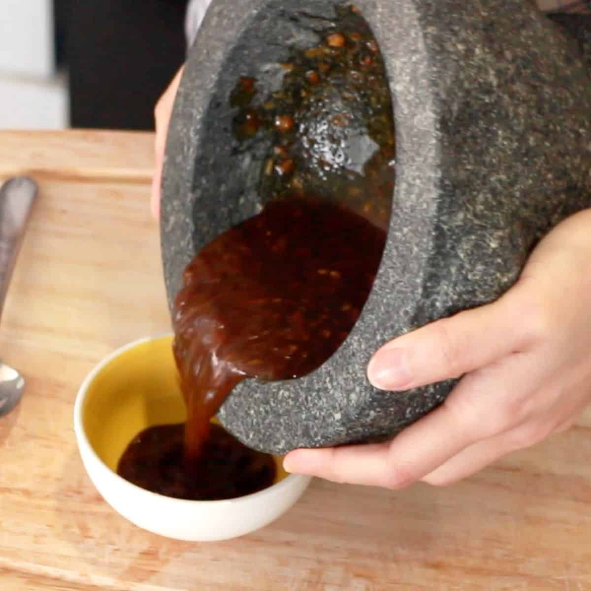 kao mun gai dipping sauce being poured from a mortar into a bowl