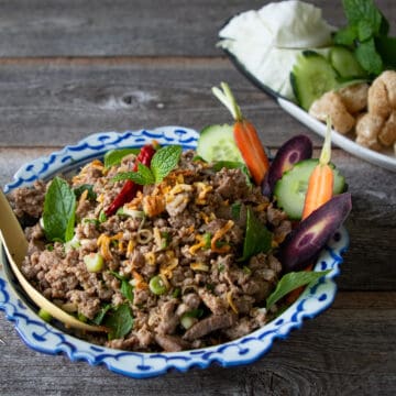 a plate of laab kua with a side of fresh veggies and more fresh veggies in the background