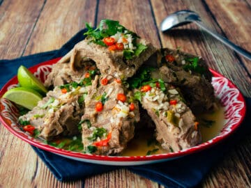 A platter of braised pork bones in a spicy garlicky broth with lime wedges on the side.