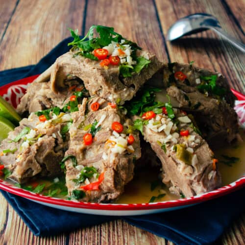 A platter of braised pork bones in a spicy garlicky broth with lime wedges on the side.