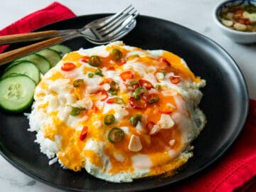 a plate of marble eggs on rice with red and green chilies on top and cucumber on the side