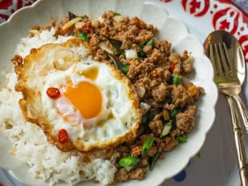 a plate of pad gaprao on rice topped with a fried egg.