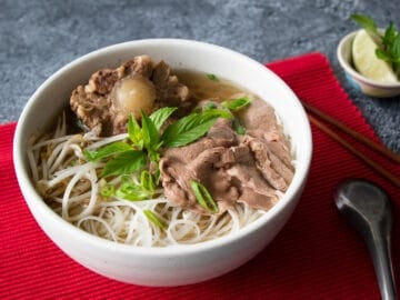 a bowl of oxtail beef pho with a lime wedge and thai basil on the side