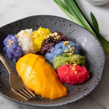 a plate of mango with 7 colours of sticky rice with mung beans on top.