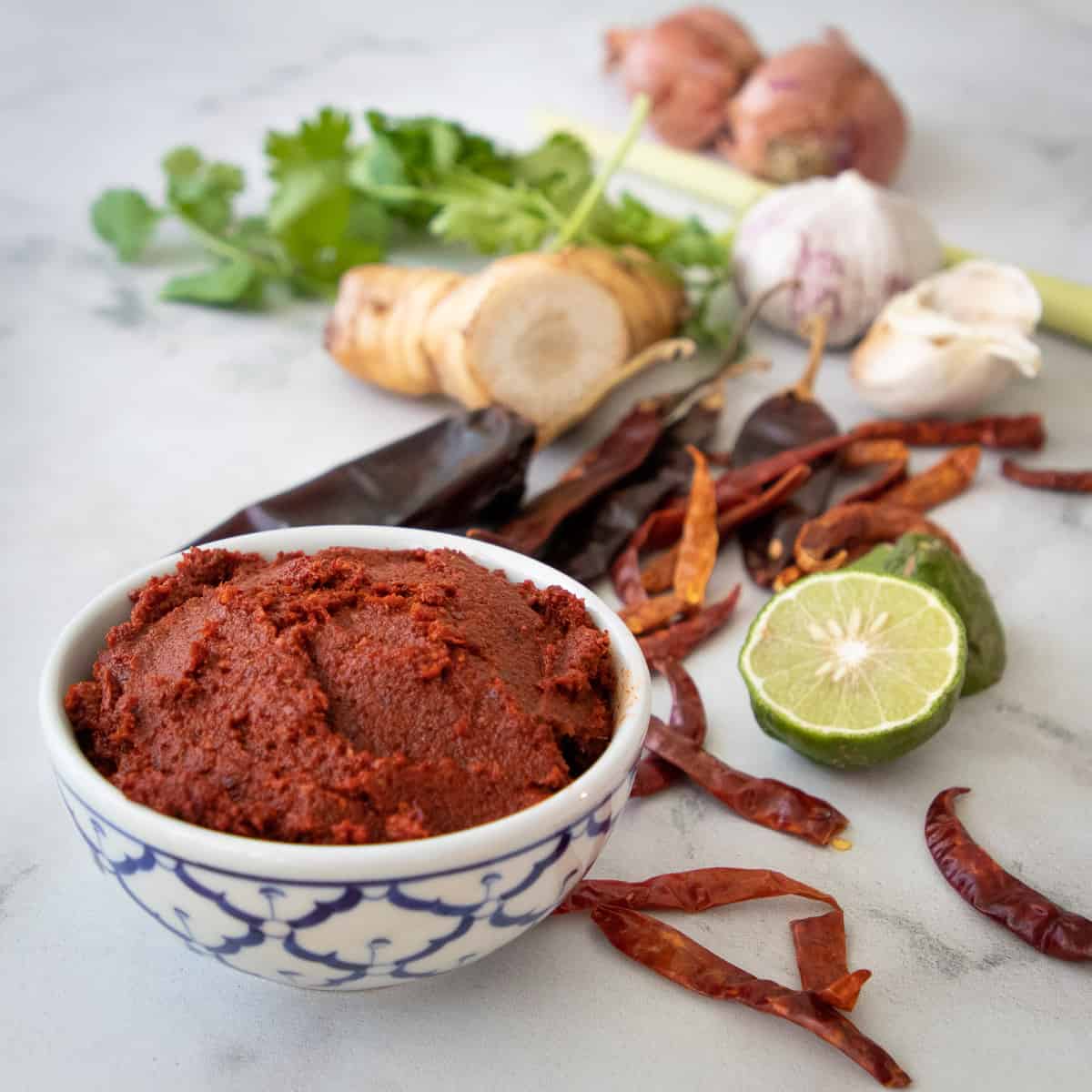 a bowl of red curry paste with ingredients in the background