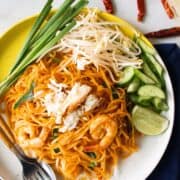 a plate of sen chan pad pu with a side of cucumber, bean sprouts and garlic chives with text overlay "Easy weeknight pad thai hot-thai-kitchen.com".