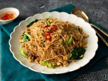 A plate of pad see ew with rice vermicelli with a side of chili vinegar