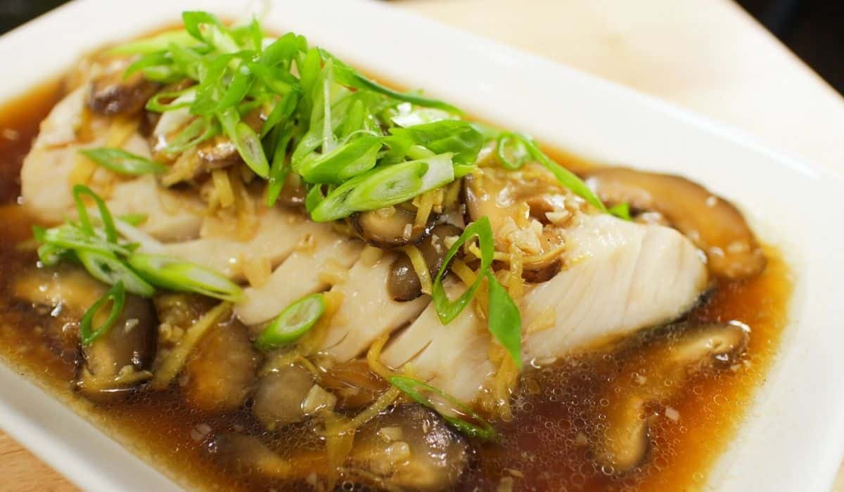 a plate of steamed black cod with ginger soy sauce and lots of green onions on top