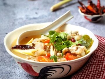 a bowl of chicken wing tom yum soup with lemongrass and chilies in the background