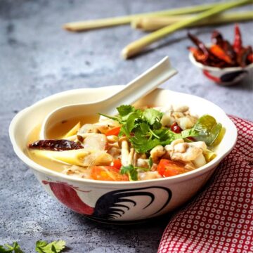 a bowl of chicken wing tom yum soup with lemongrass and chilies in the background