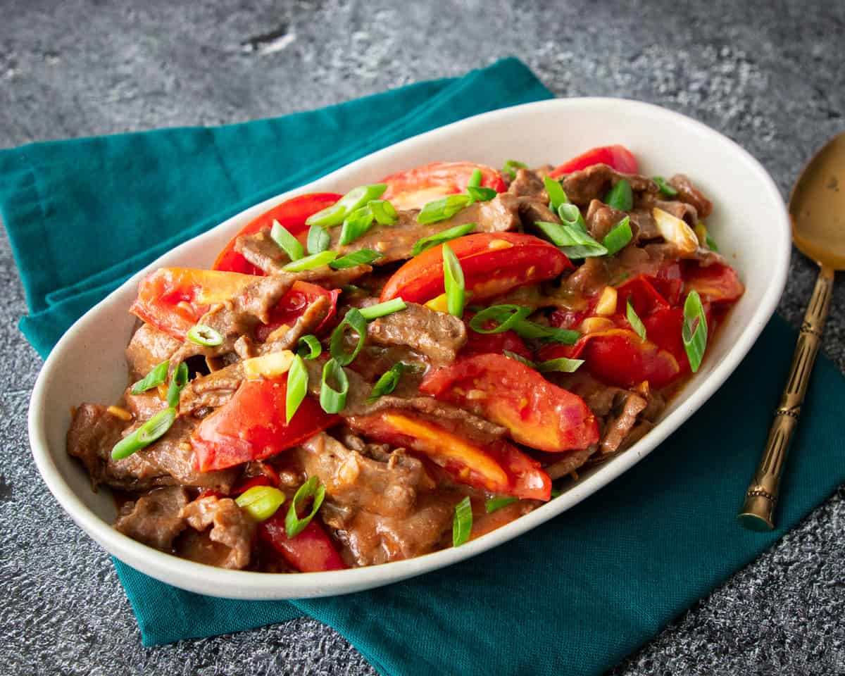 a plate of tomato beef stir fry with green onions on top