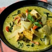 a black bowl of vegan green curry on an orange napkin with text "vegan thai green curry"