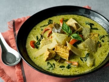 a black bowl of vegan green curry on an orange napkin