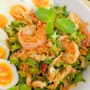 a plate of wing bean salad with boiled eggs on the side and shrimp on top.