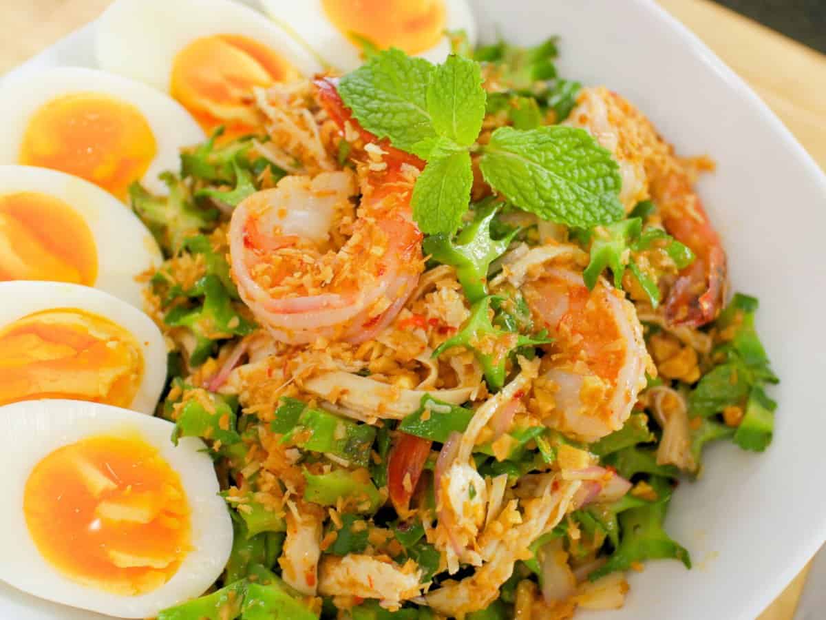 a plate of wing bean salad with boiled eggs on the side and shrimp on top.