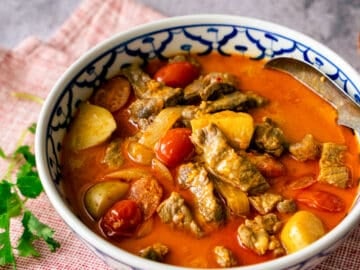 A bowl of yellow curry beef with a cilantro sprig on the side