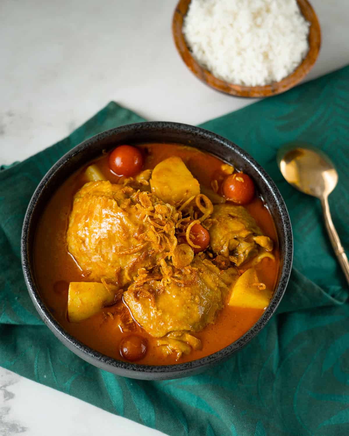 a bowl of yellow curry chicken with cherry tomatoes and potatoes and a side of rice