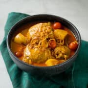a bowl of yellow curry chicken with cherry tomatoes and potatoes